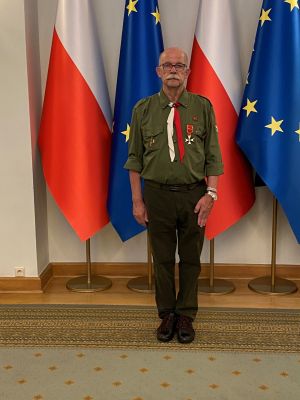 Prof. Zbigniew Pilarczyk w mundurze, z orderem, stoi na tle flag Polski i Unii Europejskiej