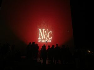 Zdjęcie z napisem Noc Naukowców wyświetlonym na ścianie budynku po zmierzchu