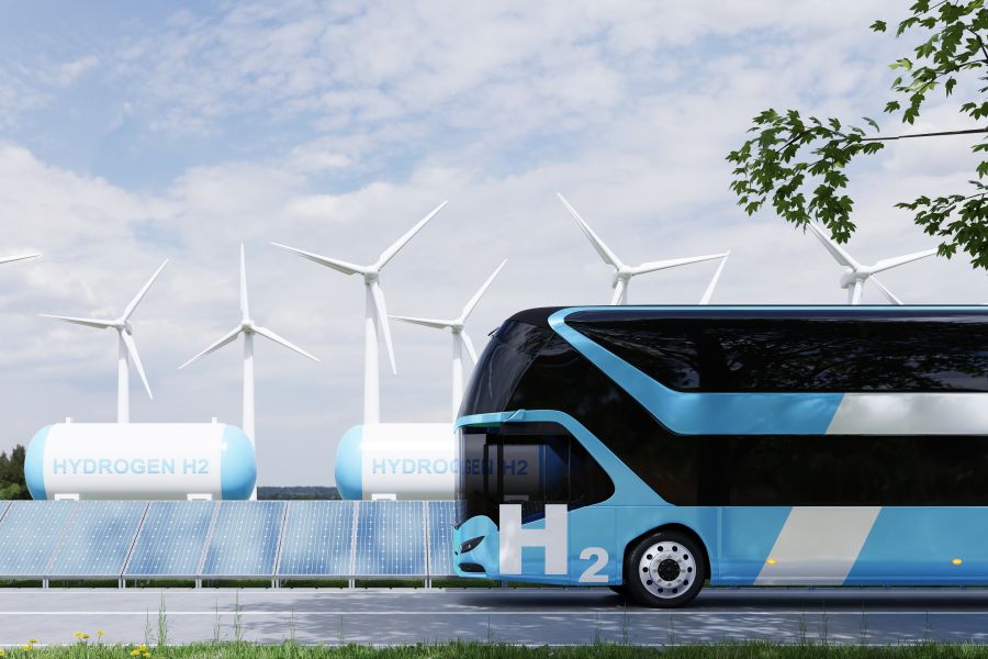 Autobus wodorowy, w tle turbiny wiatrowe i zbiorniki z gazem.