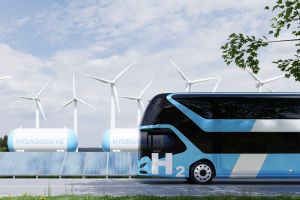 Autobus wodorowy, w tle turbiny wiatrowe i zbiorniki z gazem.