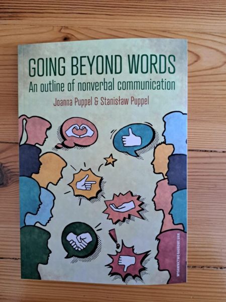 Cover of the book Going Beyond Words: An Outline of Nonverbal Communication by Joanna Puppel and Stanisław Puppel. The design shows colorful silhouettes of people with speech bubbles displaying hand gestures, facial expressions, and icons symbolizing nonverbal cues.