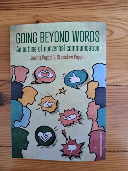 Cover of the book Going Beyond Words: An Outline of Nonverbal Communication by Joanna Puppel and Stanisław Puppel. The design shows colorful silhouettes of people with speech bubbles displaying hand gestures, facial expressions, and icons symbolizing nonverbal cues.