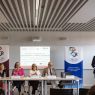 Panel dyskusyjny podczas ceremonii podpisania porozumienia; kilka osób siedzi przy stole, a jedna przemawia przy mównicy, w tle widoczna jest prezentacja „Signing Ceremony”.