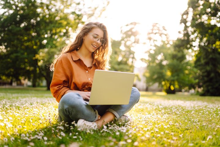 Dziewczyna siedząca na trawie, trzymająca laptopa.