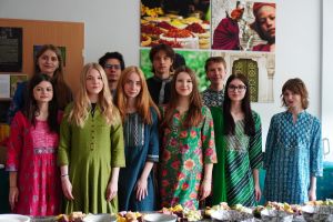 A group of students in traditional Indian clothes, standing behind the table filled with indian snacks.