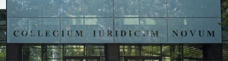 Exterior view of the Collegium Iuridicum Novum building with its glass façade reflecting surrounding trees; the name of the building is visible on the front.