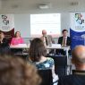 Panel dyskusyjny podczas ceremonii podpisania porozumienia; kilka osób siedzi przy stole, a jedna przemawia przy mównicy, w tle widoczna jest prezentacja „Signing Ceremony”.