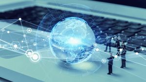 Grafika przedstawia cyfrowy glob ziemski unoszący się nad klawiaturą laptopa, otoczony siatką połączeń i ikon symbolizujących technologie i komunikację. W tle widoczne są miniaturowe sylwetki ludzi.