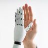 Dłoń człowieka zestawiona z białą robotyczną dłonią na jasnym tle.
