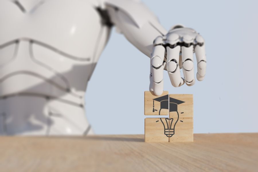 Robotyczna dłoń układająca drewniane klocki z grafiką żarówki i biretu akademickiego, symbolizującą połączenie sztucznej inteligencji i edukacji.