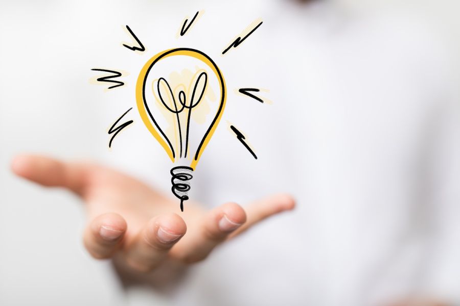 Rysunkowa żarówka unosząca się nad wyciągniętą dłonią osoby w białej koszuli, symbolizująca pomysł.