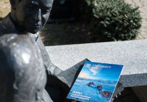 University Life magazine featuring AMU Polar Station Petuniabukta placed on a sculpture of reading figures in an outdoor setting