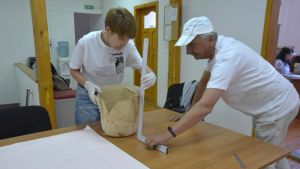 Prof. Elena Klenina and Prof. Andrzej B. Biernacki measure an ancient chamber pot placed on a table
