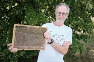 Prof. UAM Adam Głazaczow trzymający ramkę z ula. W tle drzewo liściaste.