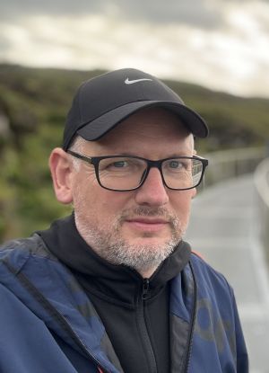 Portrait photograph showing Dr Robert de Louw wearing a black cap against a blurred background