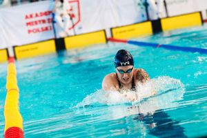 Pływaczka płynie stylem klasycznym w basenie sportowym podczas zawodów.