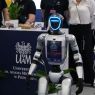 Zbliżenie na humanoidalnego robota stojącego przed stoiskiem Uniwersytetu im. Adama Mickiewicza; w tle widoczne są materiały promocyjne i osoby przy stoisku targowym.