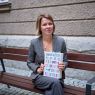The pictures shows prof. Emilia Kledzik sitting on the bench in front of the AMU Faculty of Polish and Classical Philology. She holds her awarded book in her hands. 