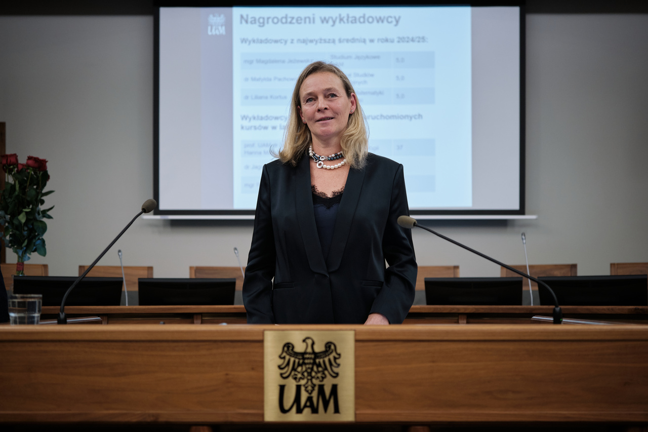 Kobieta stojąca przy mównicy z logo Uniwersytetu im. Adama Mickiewicza w Poznaniu