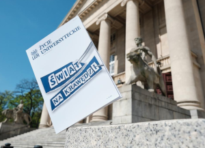 Okładka pisma „Życie Uniwersyteckie” z hasłem „Świat na krawędzi”, sfotografowana na tle schodów i kolumn budynku.