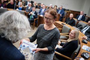 Kobieta odbiera dyplom z napisem „Uniwersytet Otwarty” podczas uroczystości w sali Uniwersytetu im. Adama Mickiewicza w Poznaniu. W tle widać publiczność siedzącą w ławkach