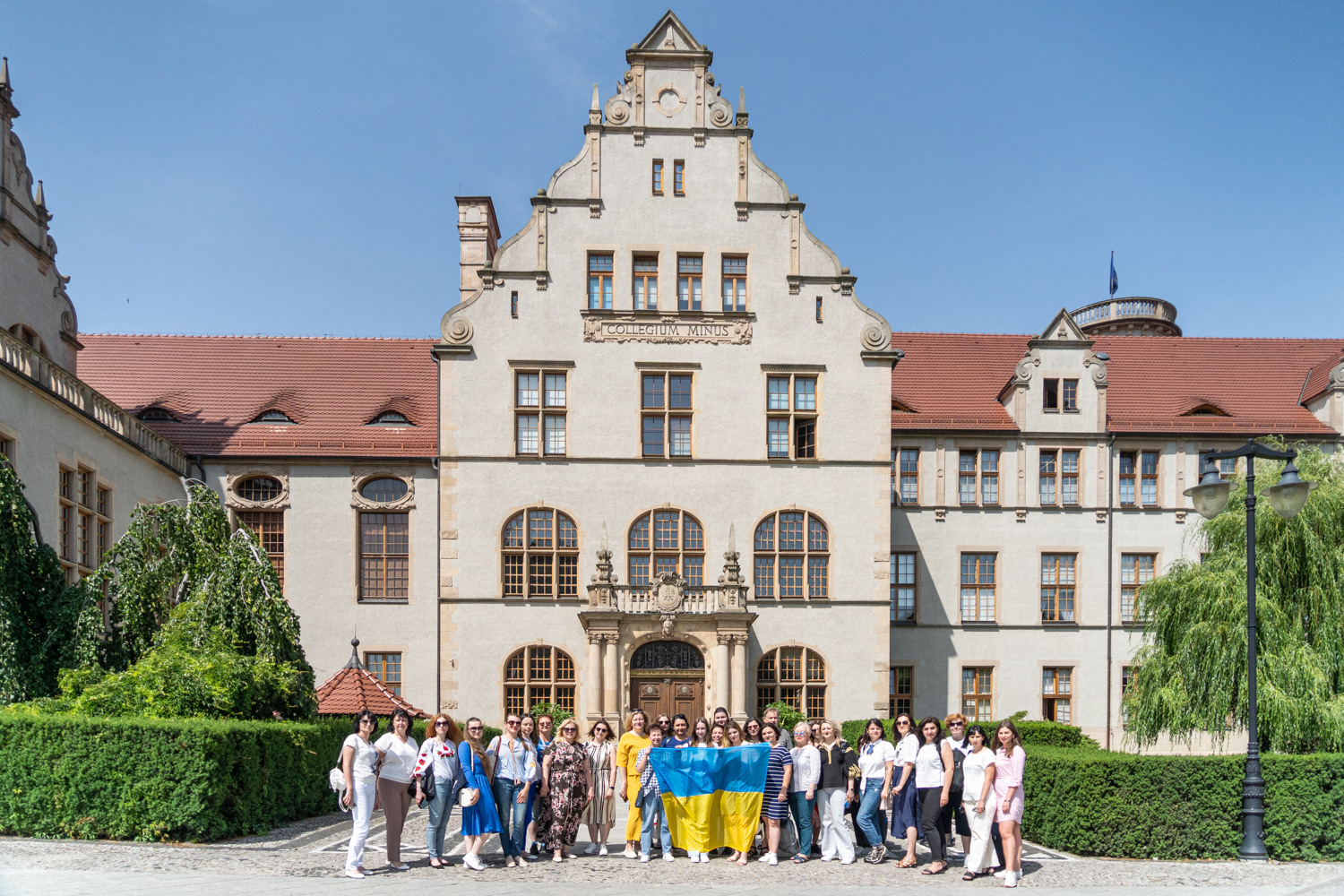 Group photo from AMU's summer school, in front of Collegium Minus. Participants hold a Ukrainian flag.